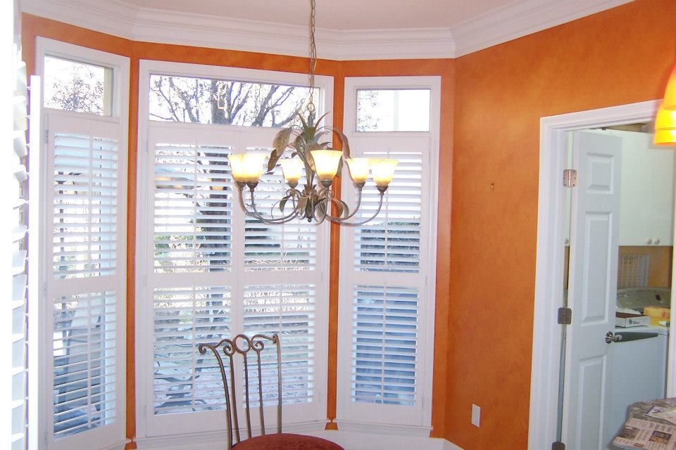 Bay window with white shutters, orange walls, chandelier, chair. Interior shot.