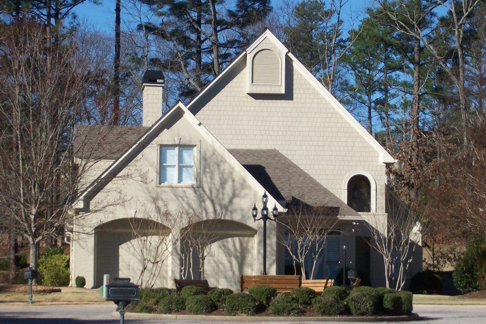 Tan and beige house with arched garage, trees, and blue sky.