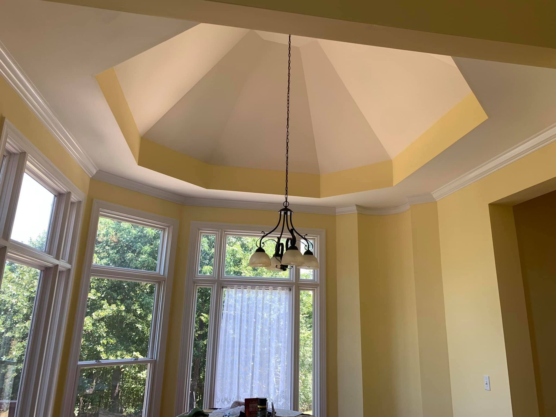 Interior view of a room with a multi-angled ceiling, yellow walls, white trim, and a chandelier.