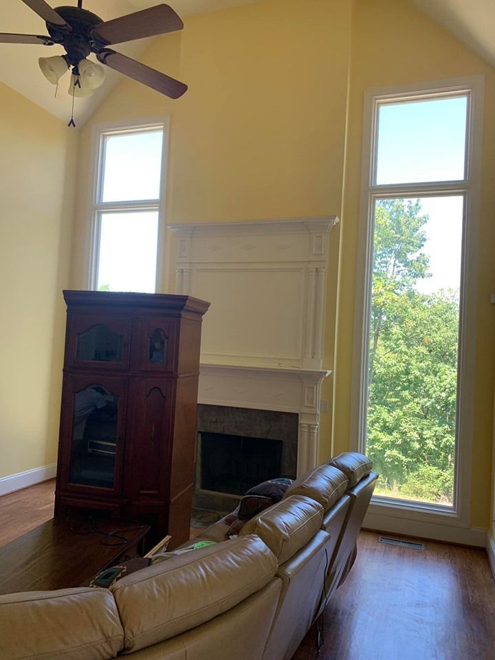 Living room with tall windows, fireplace, tan walls, dark wood furniture, and a light-colored sofa.