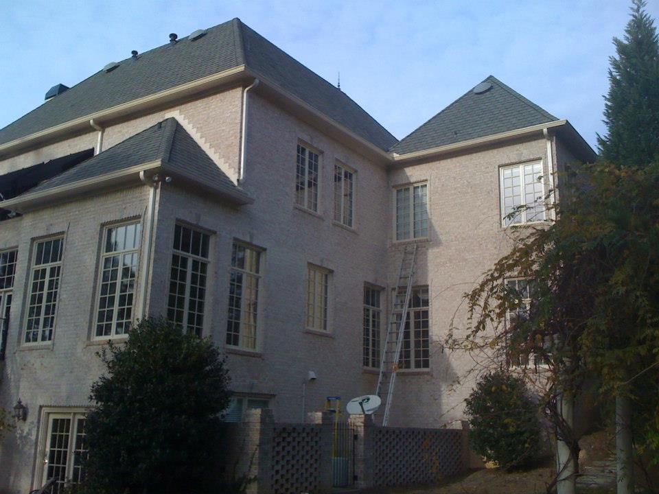 Beige stucco house with dark green roof, multiple windows, and ladder against the wall.