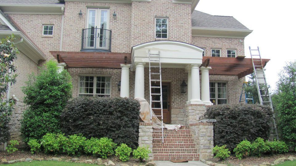 A brick home exterior with a porch, two ladders, and workers.