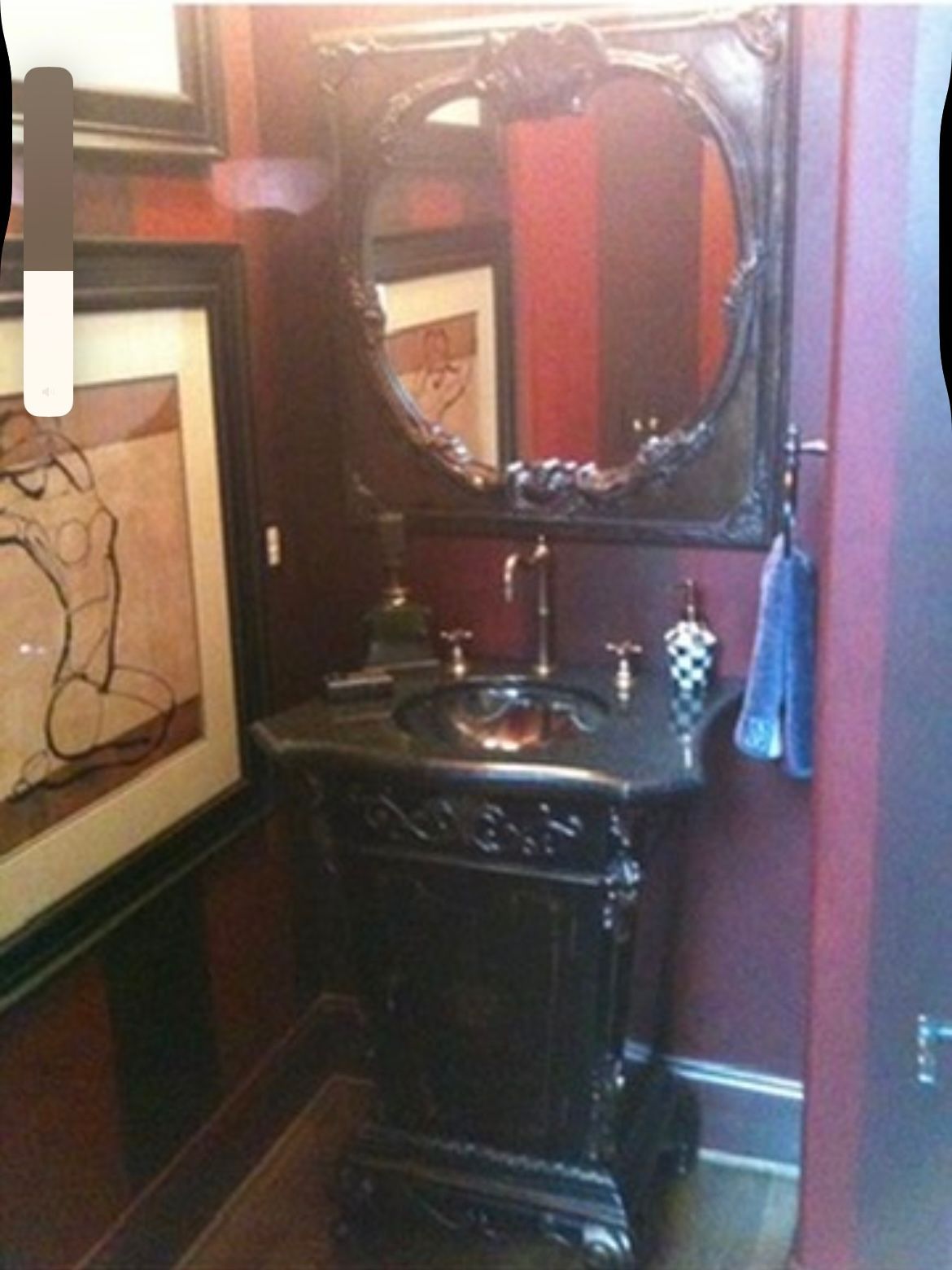 Elegant black vanity with ornate details, oval mirror, artwork, and red striped wall.