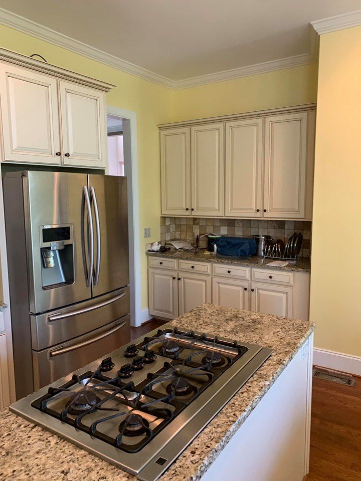 Kitchen with stainless steel refrigerator, gas cooktop, and off-white cabinets against yellow walls, on a wooden floor.