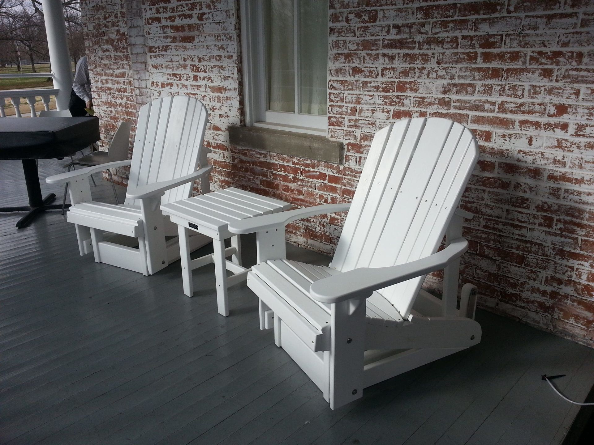 Two white adirondack chairs and a table on a porch