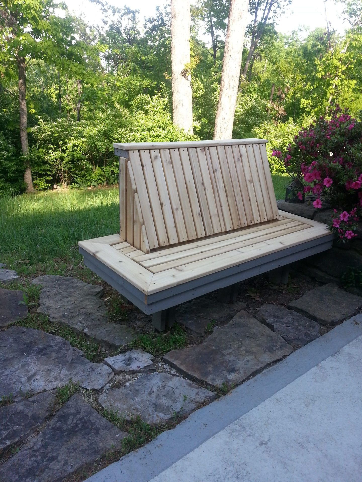 A wooden bench is sitting on a stone patio in front of trees