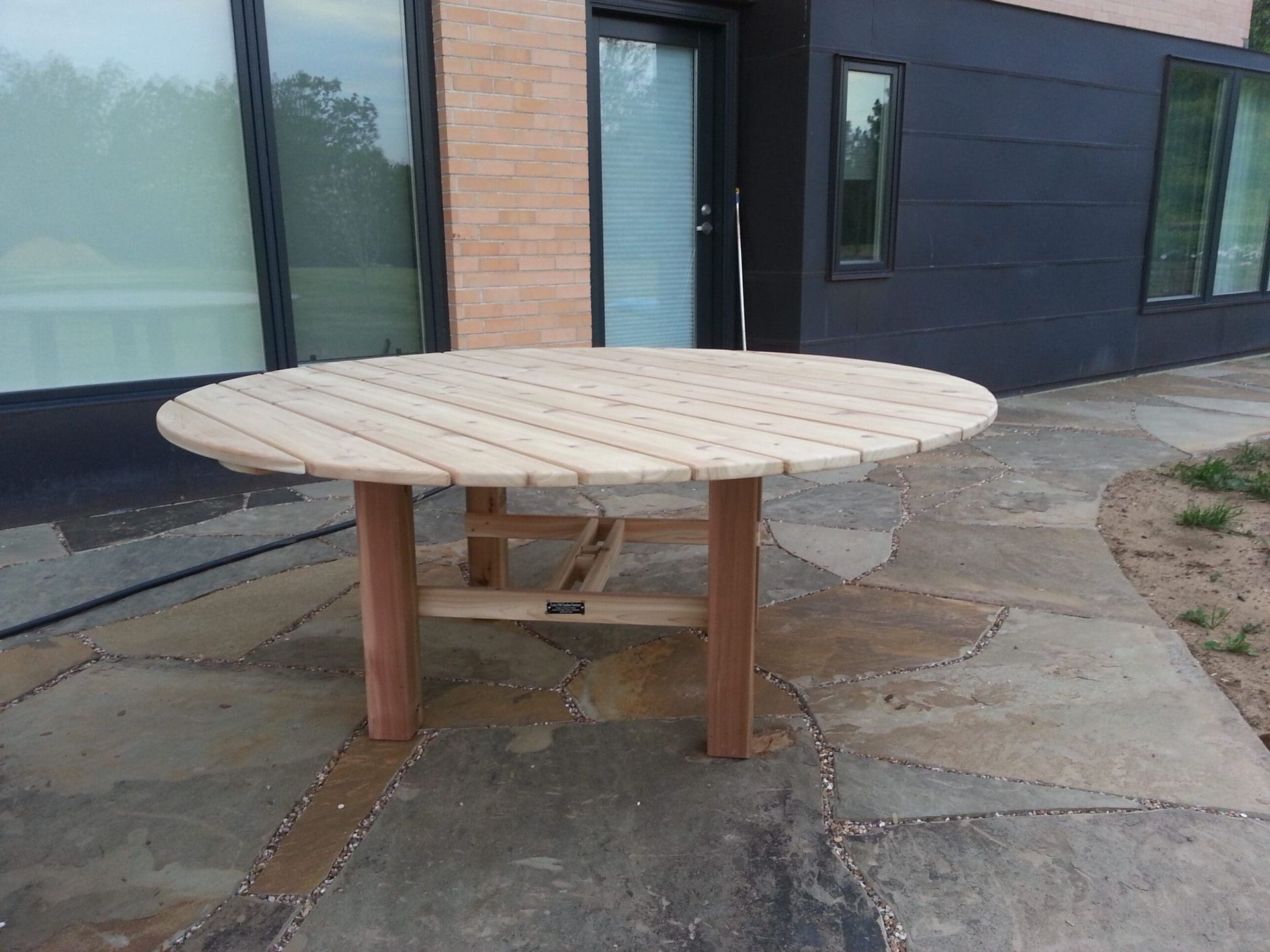 A round wooden table is sitting on a stone patio in front of a building