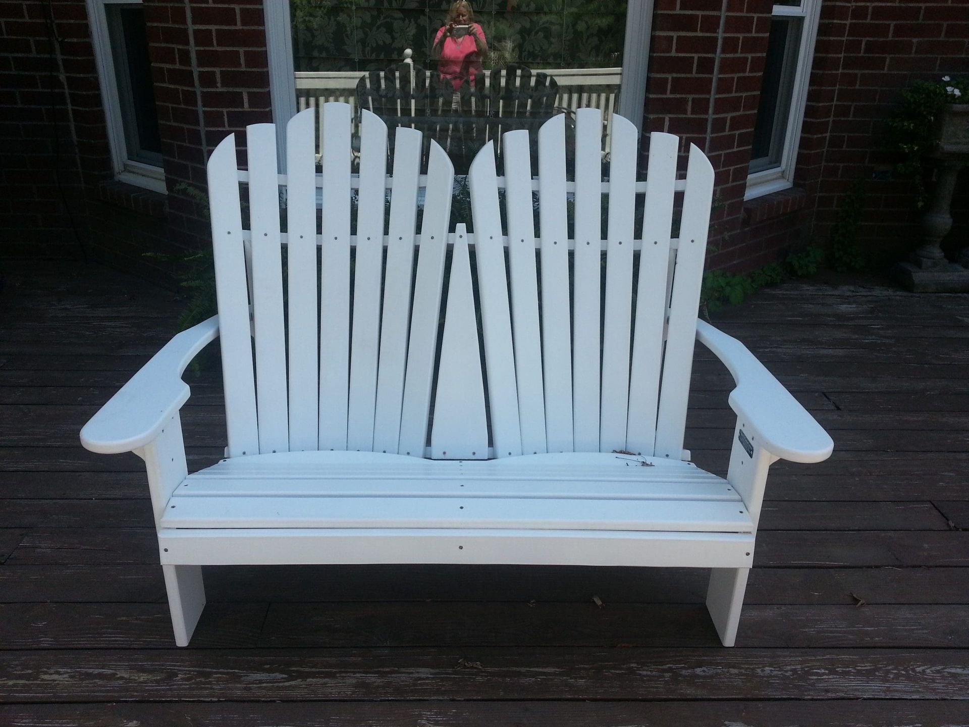 A white wooden bench sits on a wooden deck in front of a brick building