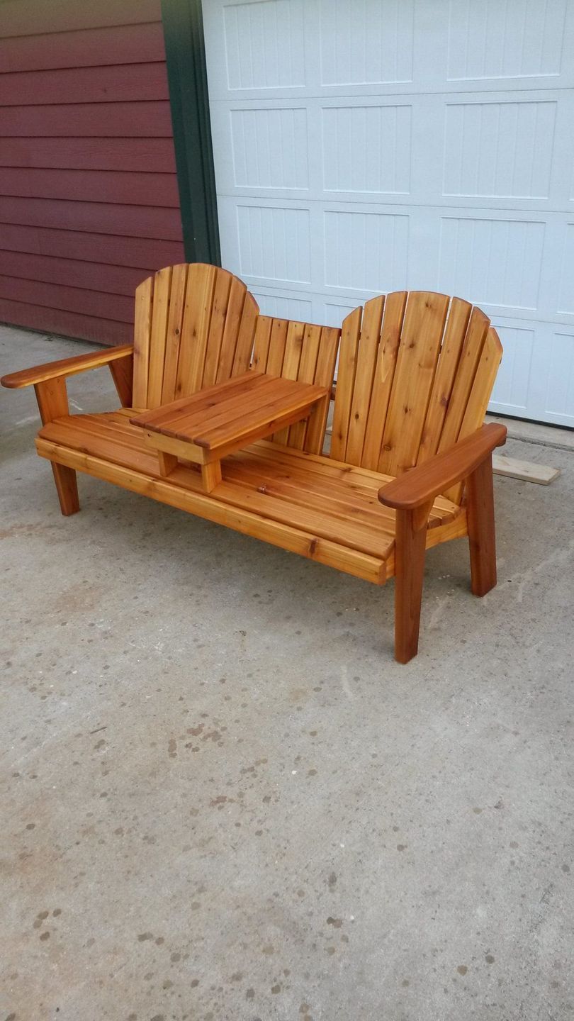 A wooden bench with two chairs and a table in front of a garage door.