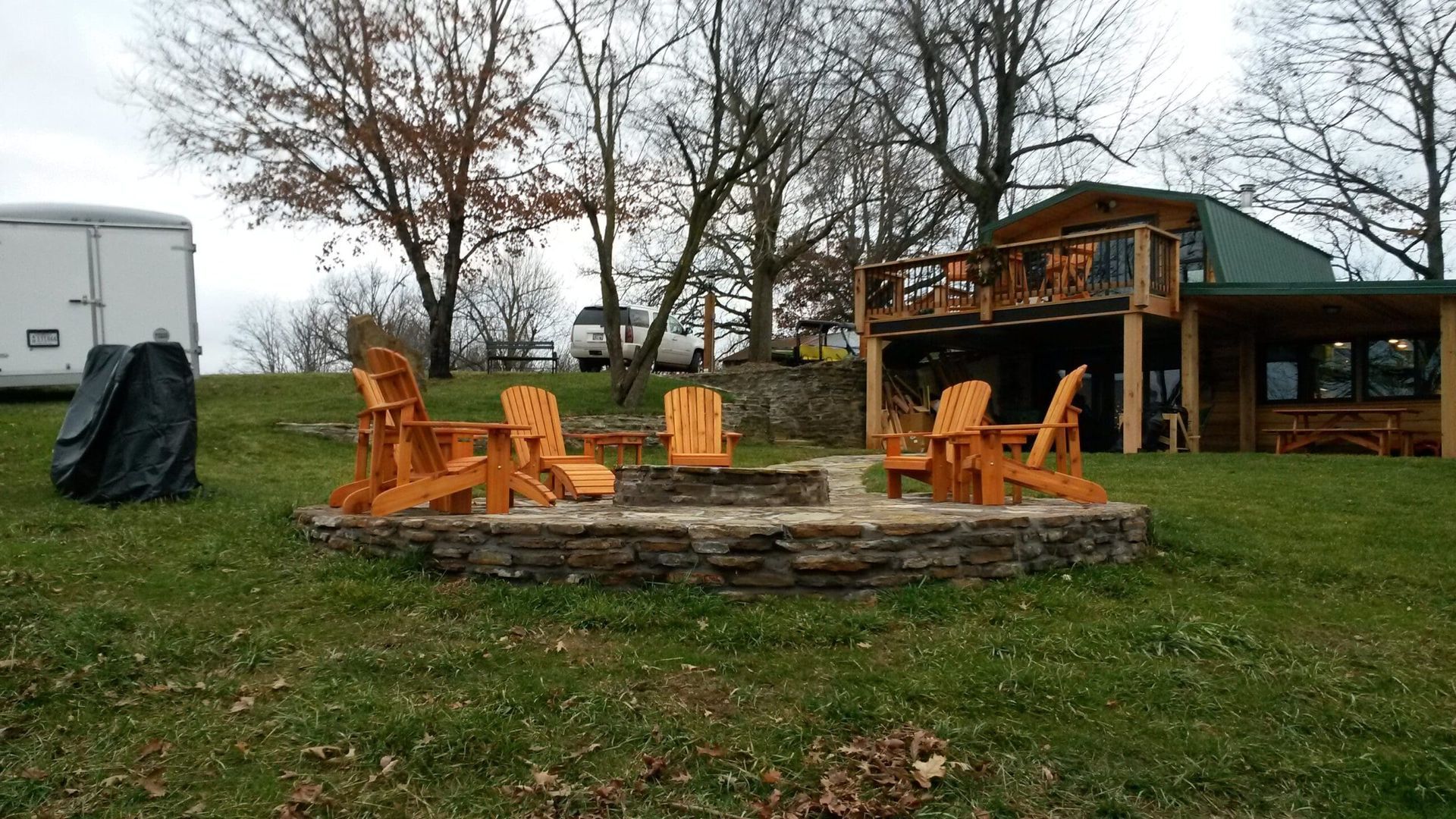 A fire pit with wooden chairs in front of a cabin.