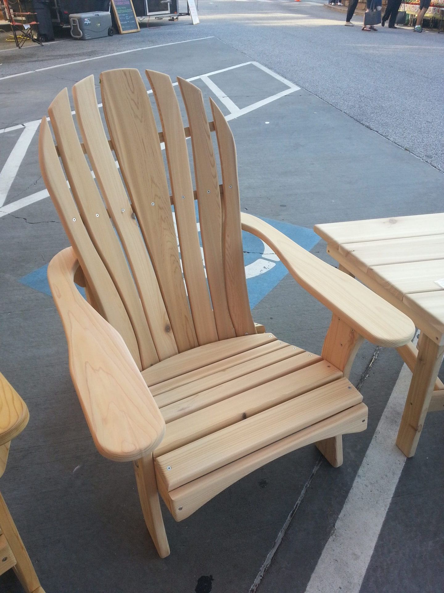 A wooden chair is sitting in a parking lot next to a table.