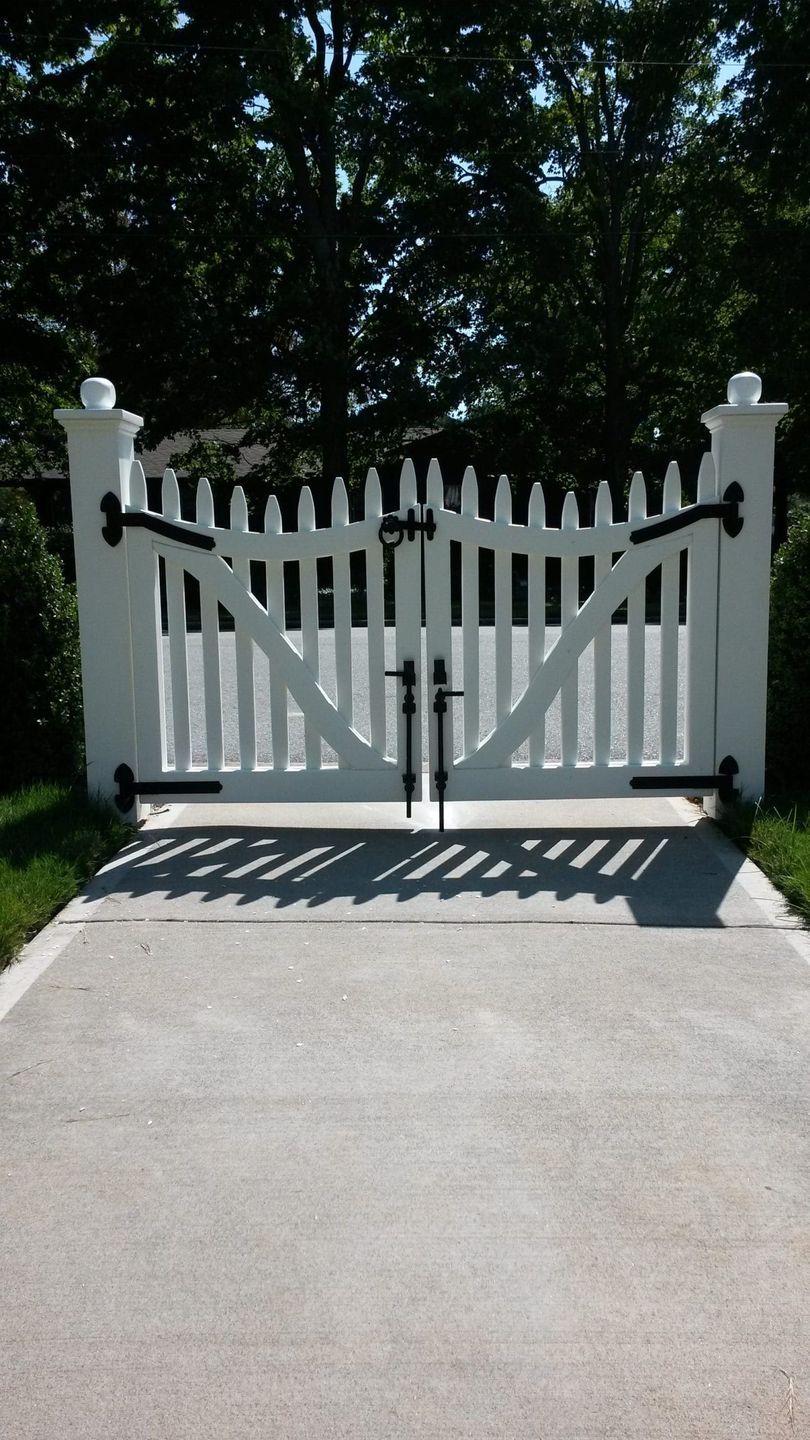 A white picket gate is open to a driveway