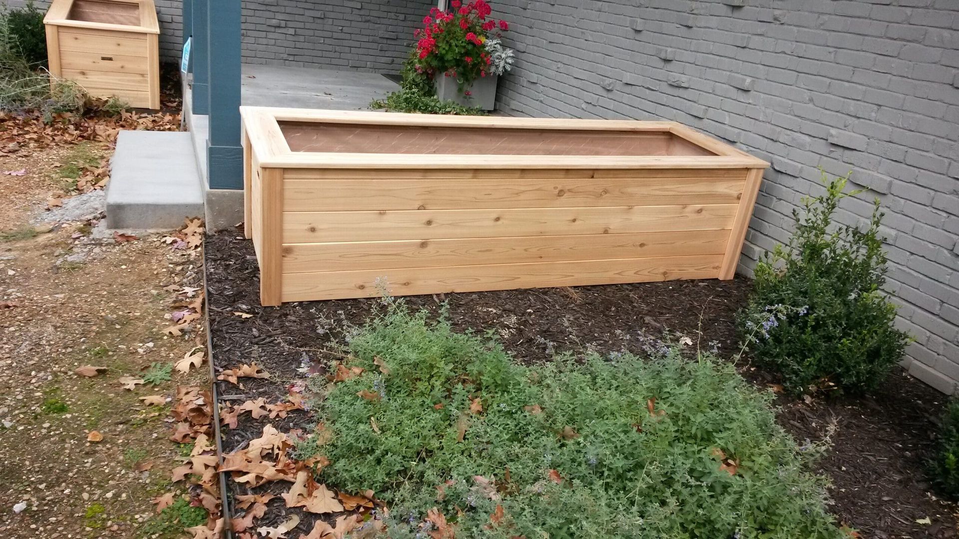 A wooden planter is sitting in a garden next to a brick wall.