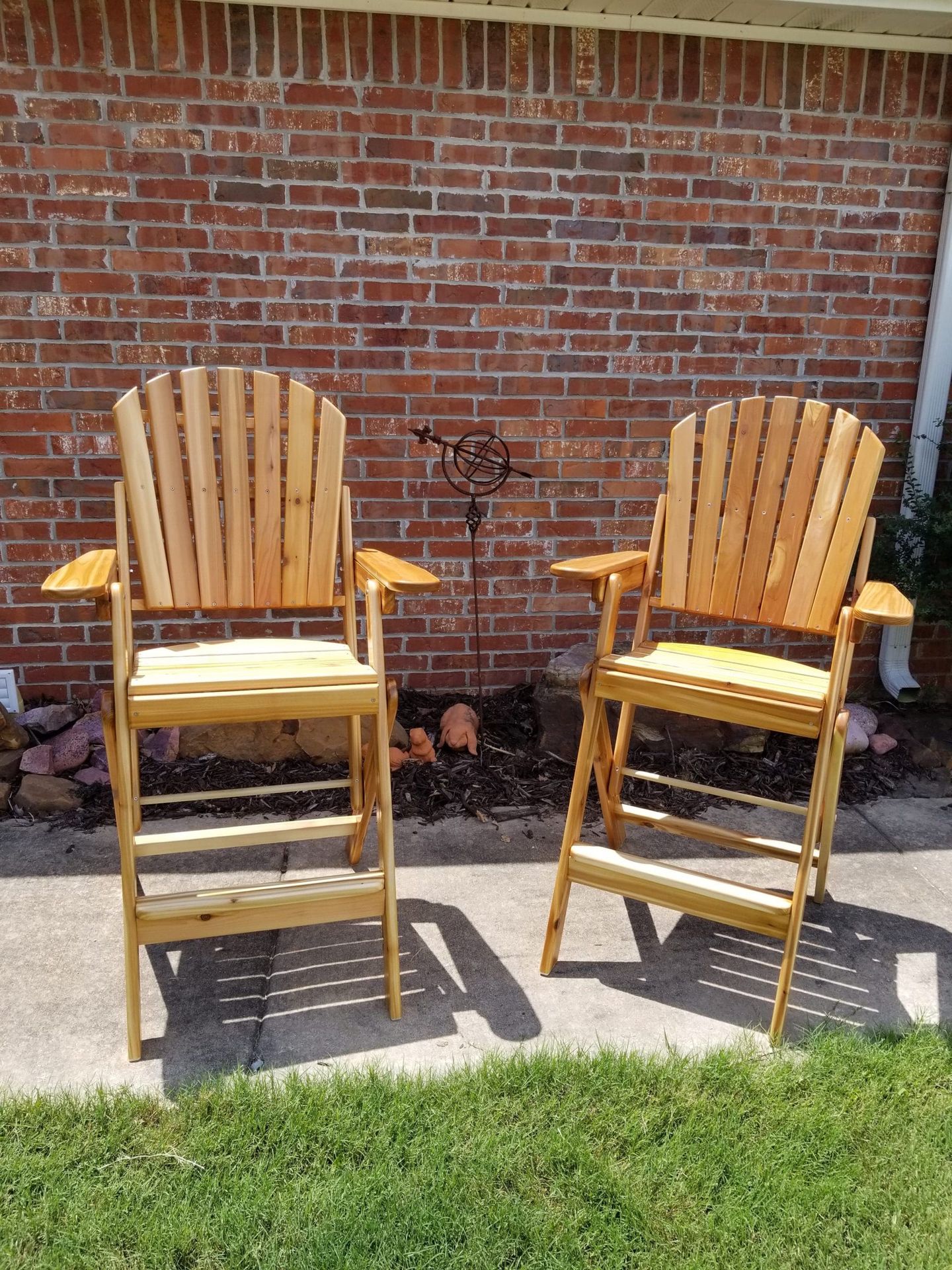 Two wooden chairs are sitting on a sidewalk in front of a brick wall.