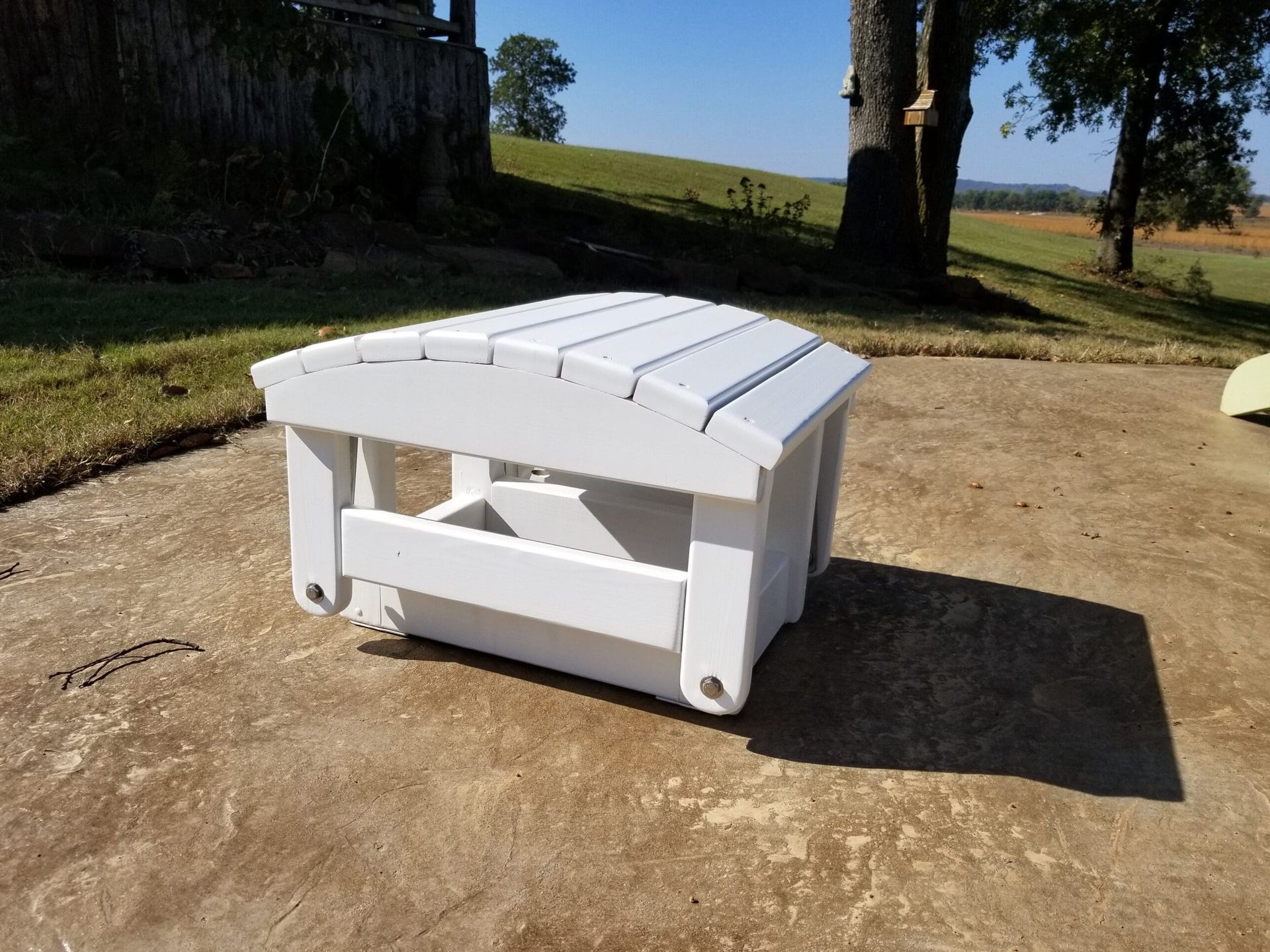 A white wooden ottoman is sitting on a concrete surface.