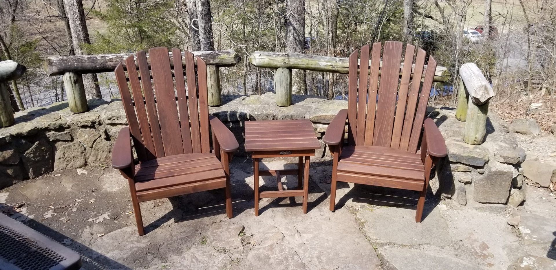 Two wooden adirondack chairs and a table are sitting on a patio.