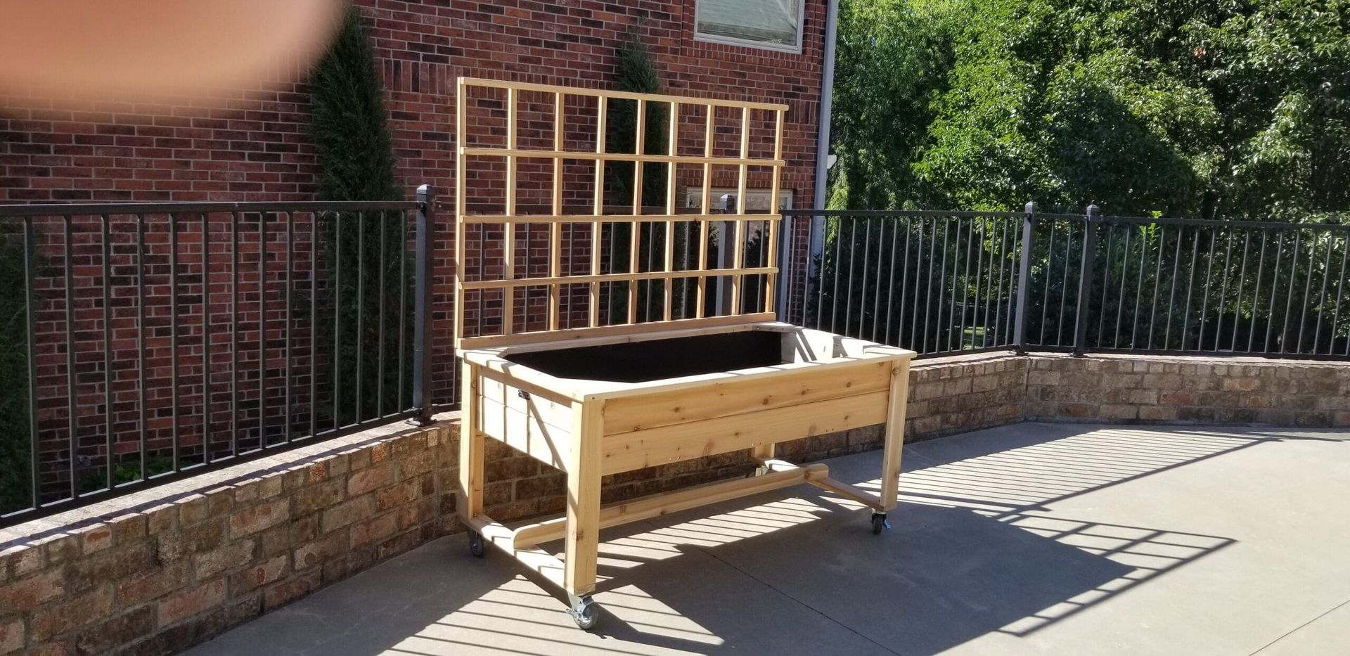 A wooden planter is sitting on a patio next to a brick wall.