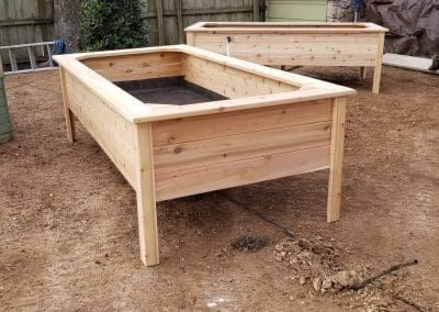 Two wooden raised garden beds are sitting on top of a dirt field.