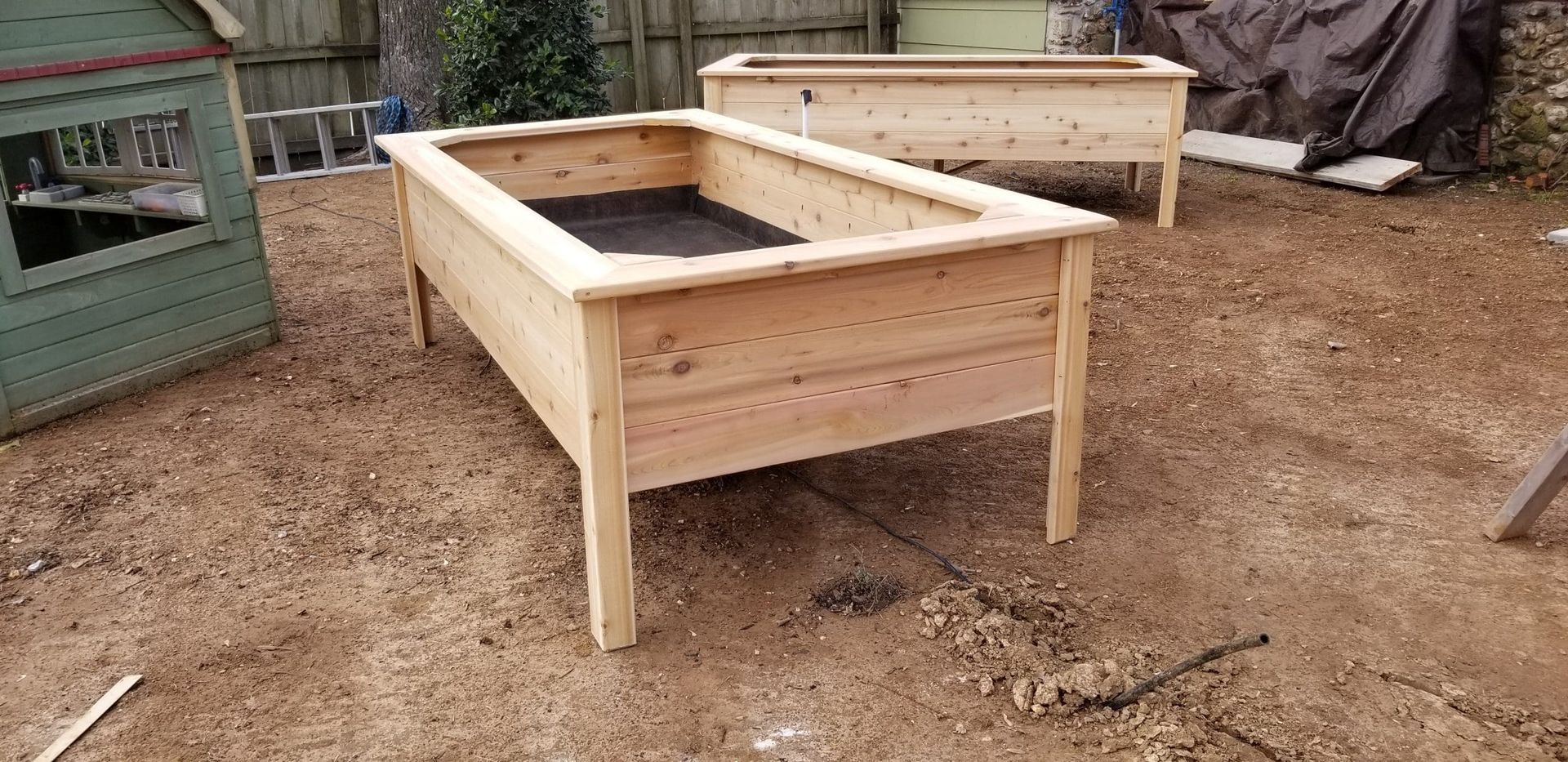 Two wooden planters are sitting on top of a dirt field.