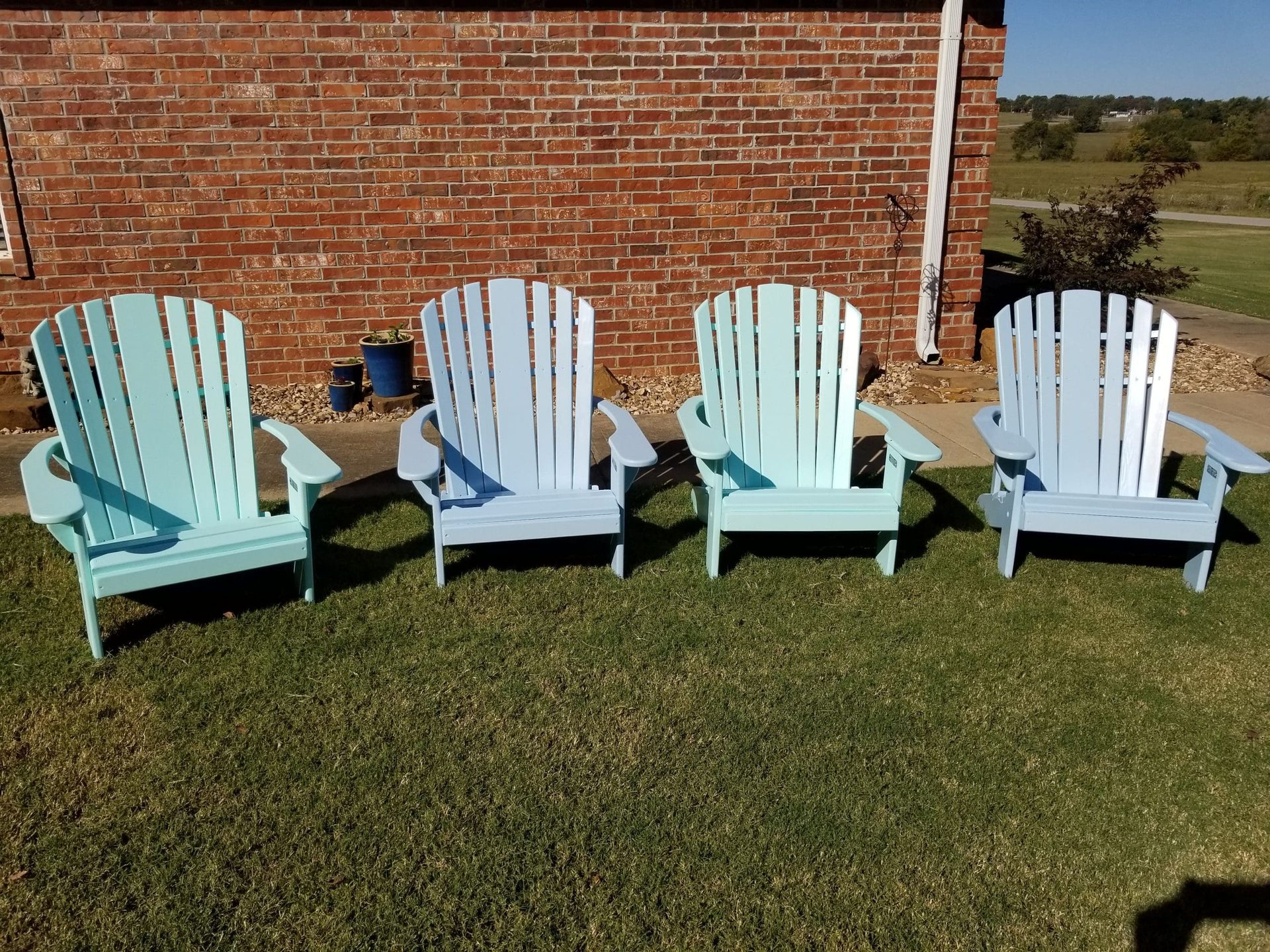 Four lawn chairs are lined up in a row in front of a brick wall.