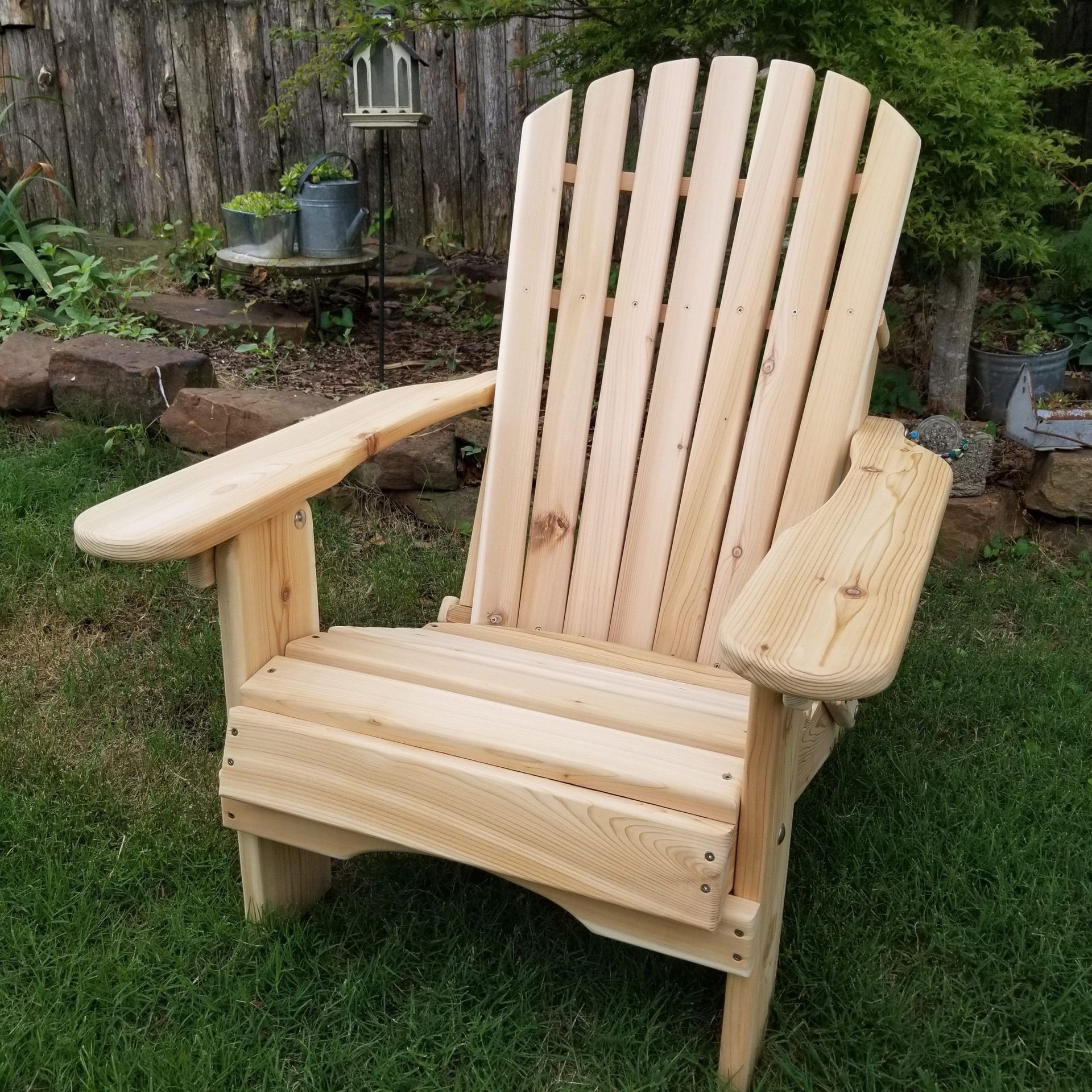 A wooden adirondack chair is sitting in the grass