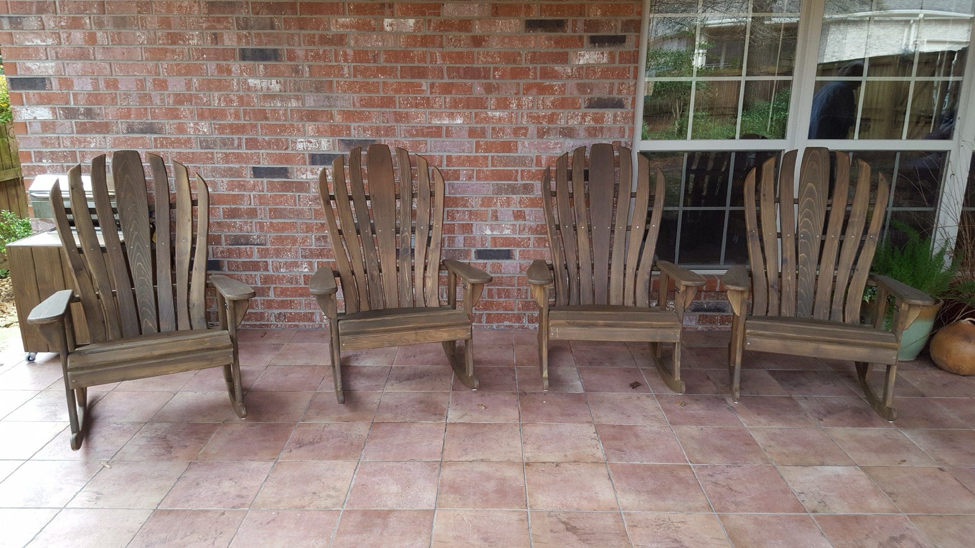 A row of wooden chairs are sitting on a tiled patio in front of a brick wall.