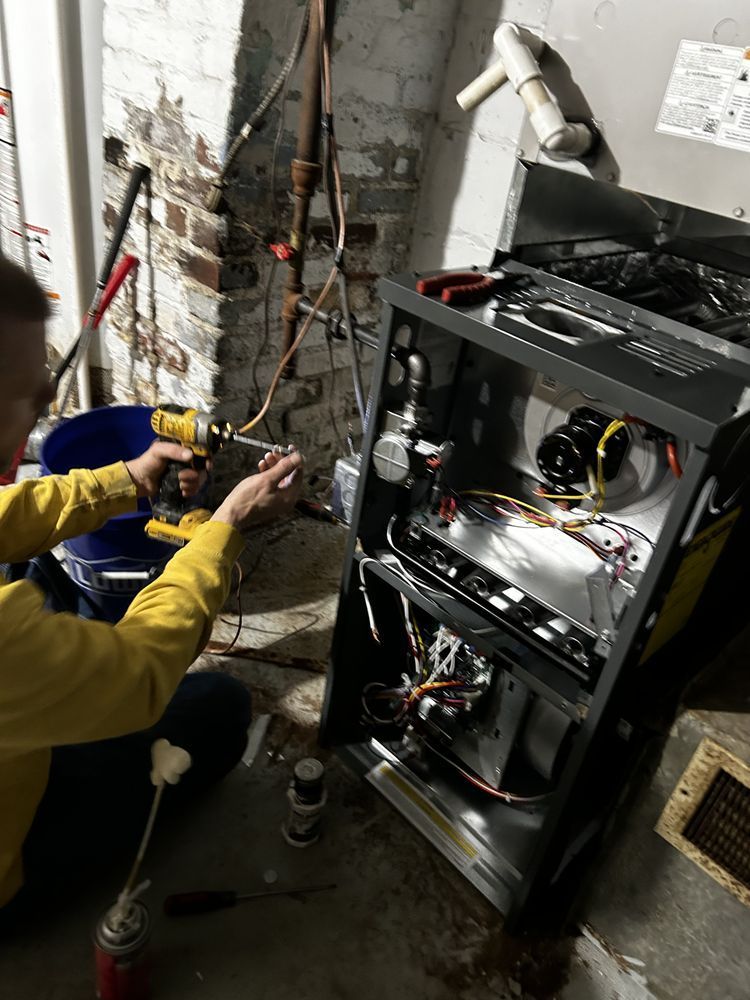 Person using a drill to work on a furnace in a basement setting.