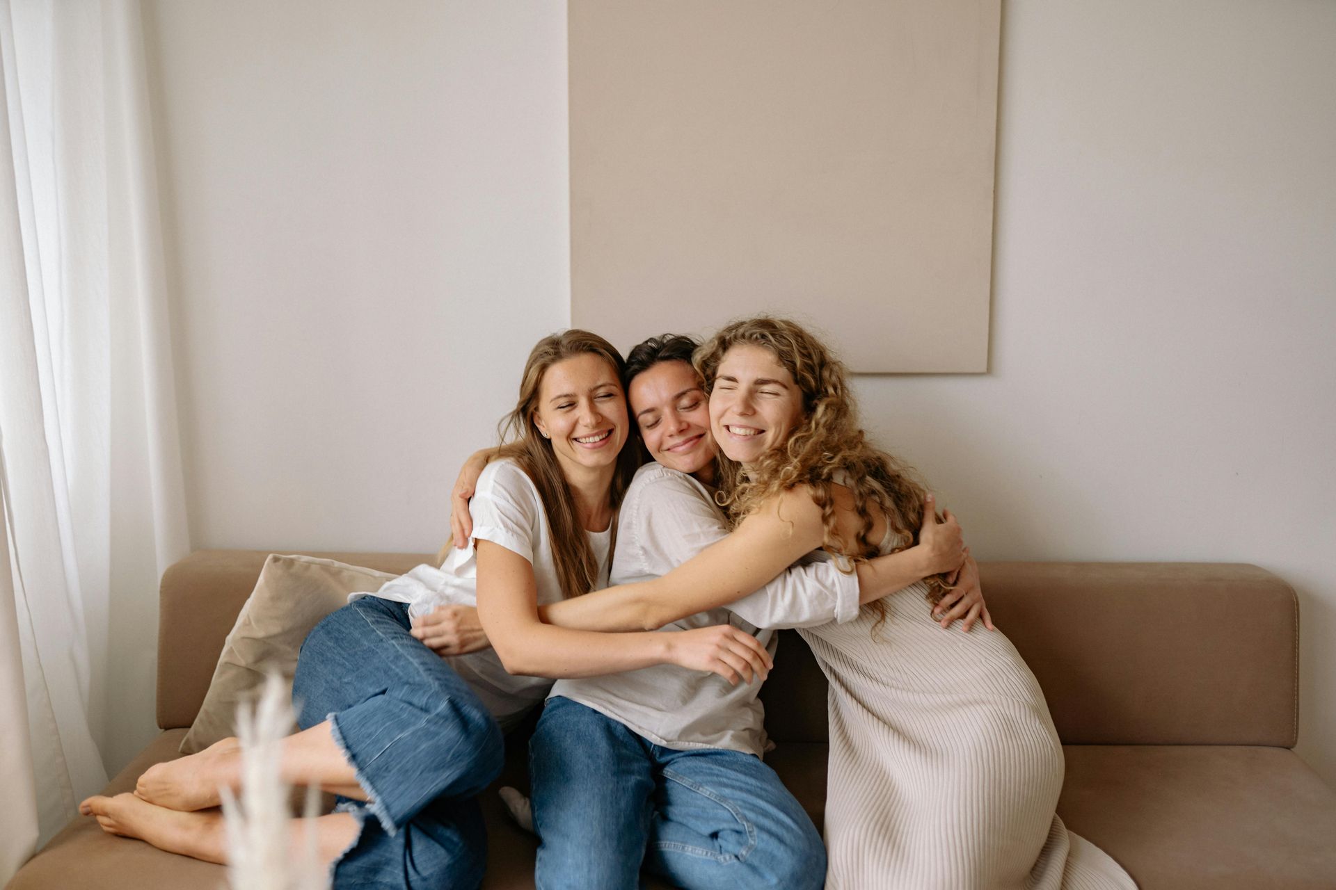 Three people hugging on a couch; one has curly hair, all smiling.