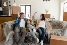 Family in new home, cheering on sofa surrounded by moving boxes.