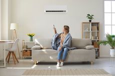 Woman using remote control for air conditioner in a bright living room.