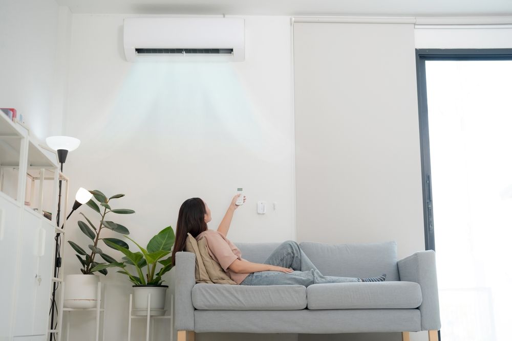 Woman reclining on a couch, using a remote to control the air conditioner above.