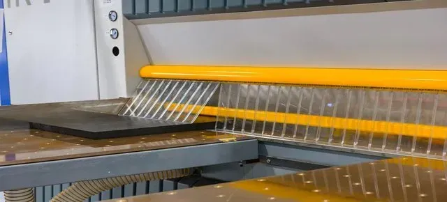 Industrial panel saw with a yellow guard and transparent safety curtain positioned over a work table.