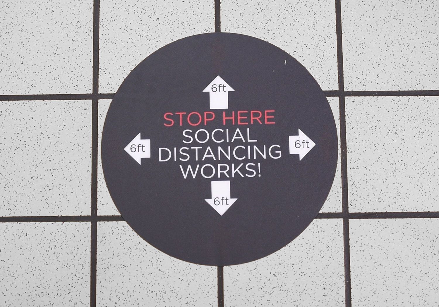 A sign on the floor that says stop here social distancing works