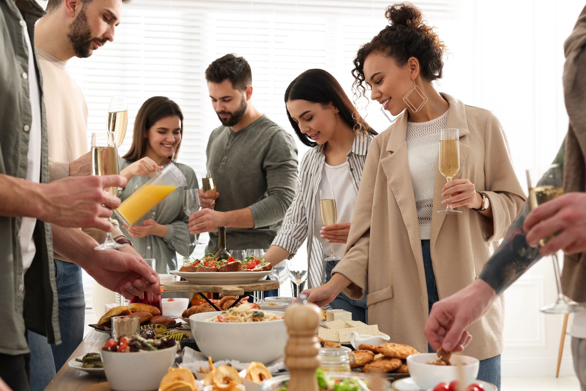 A group of people are standing around a table eating food and drinking champagne.
