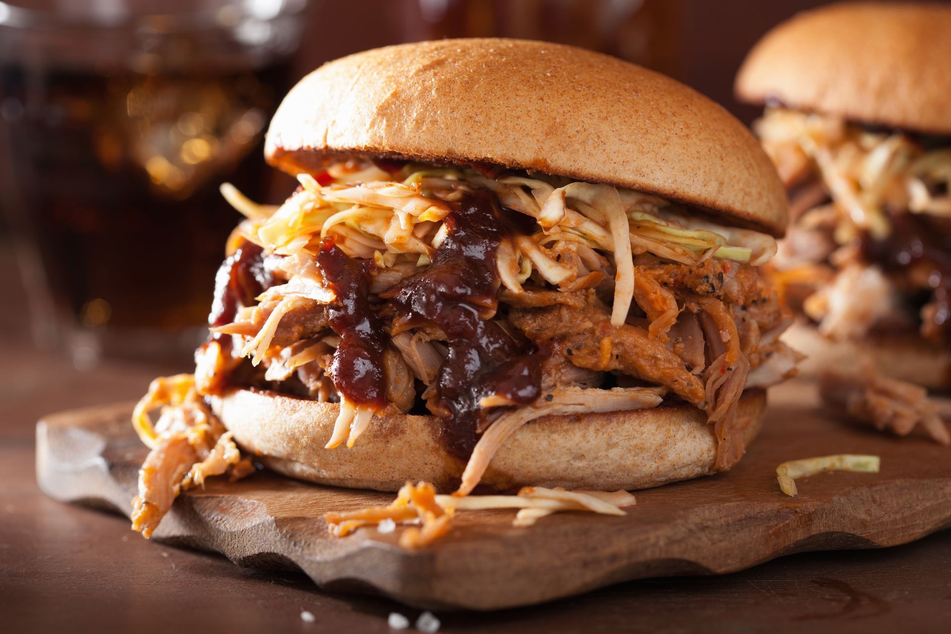 A pulled pork sandwich is sitting on a wooden cutting board.