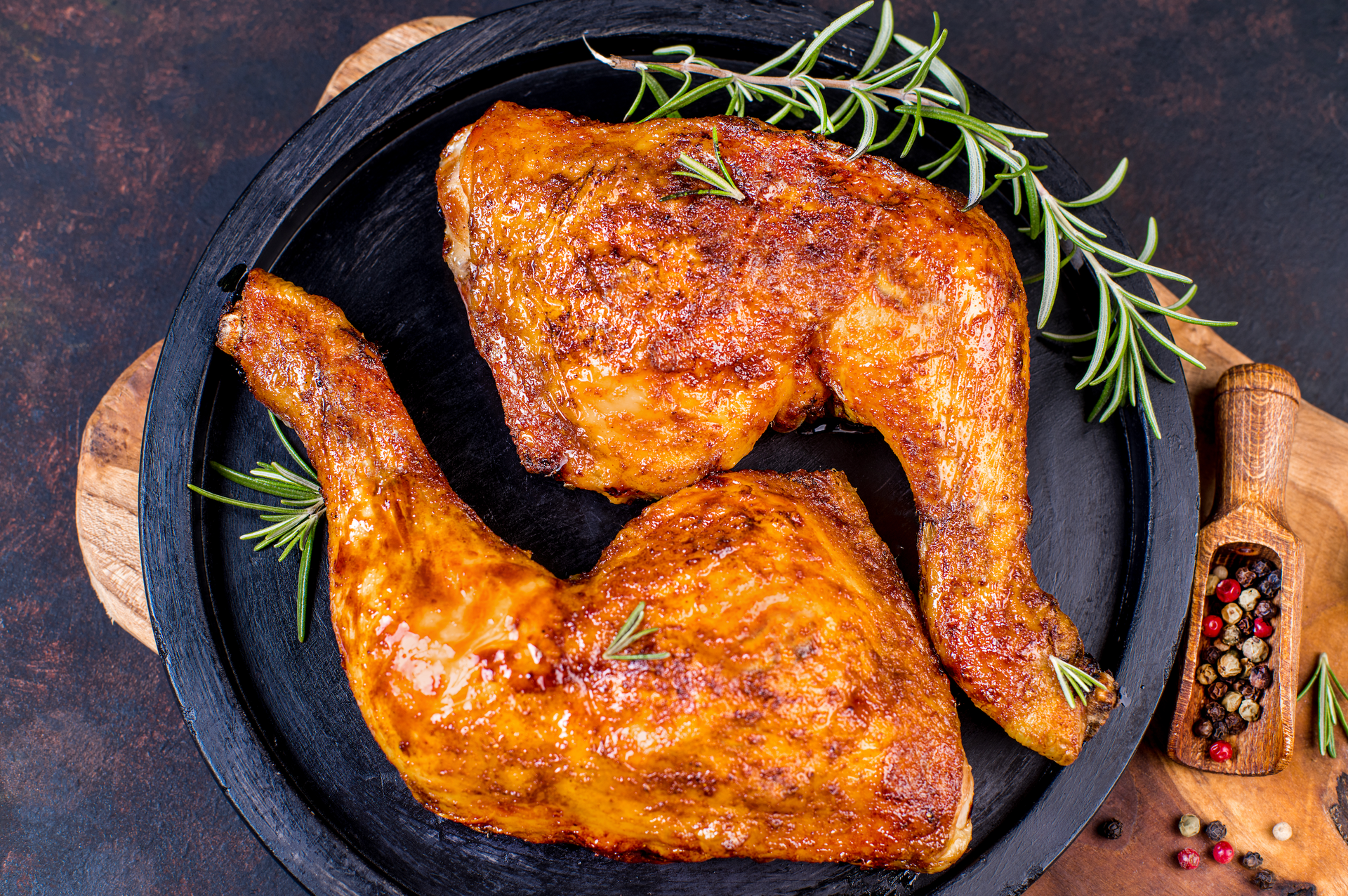 Two pieces of grilled chicken on a black plate with rosemary.