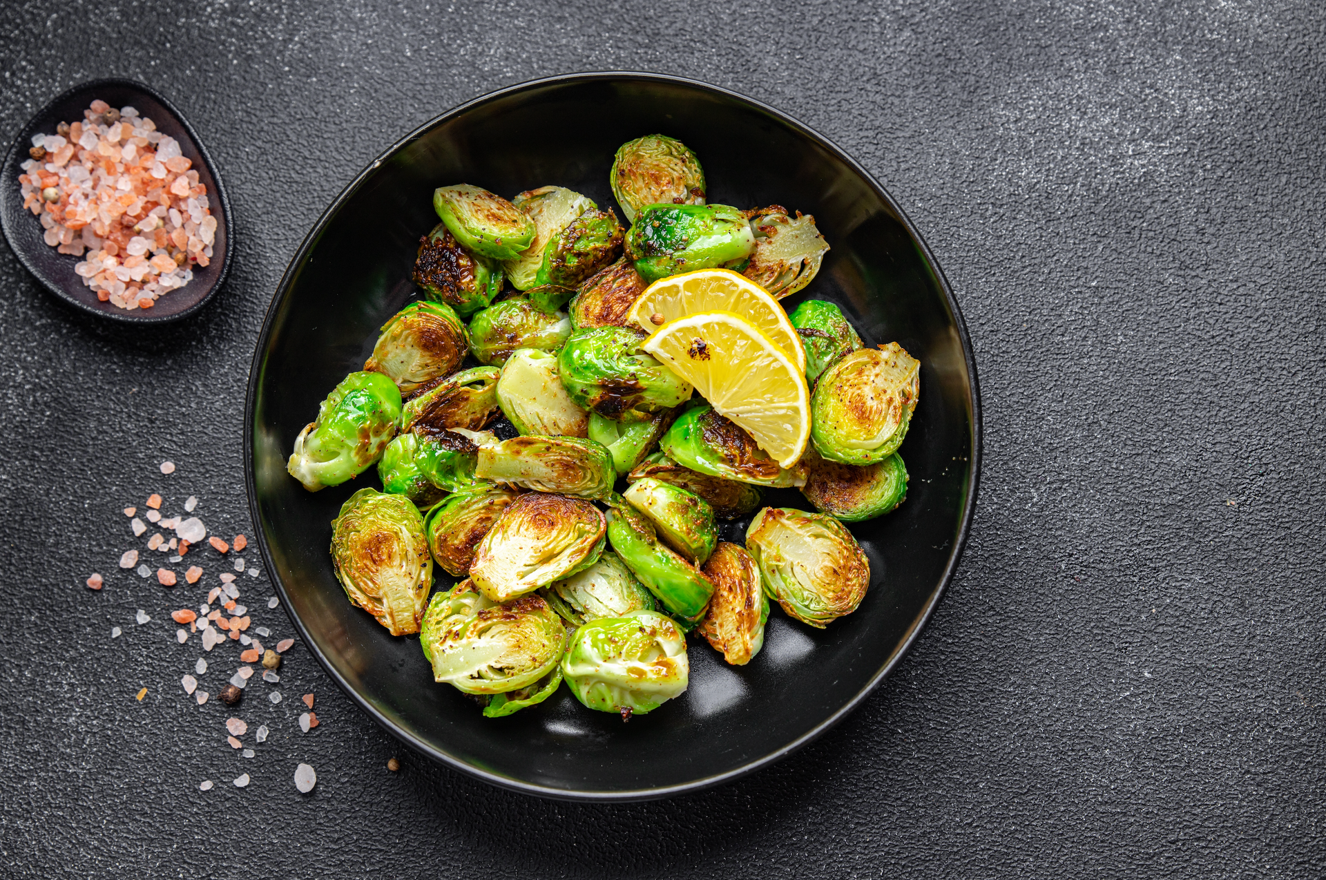 A black bowl filled with brussels sprouts and lemon slices.