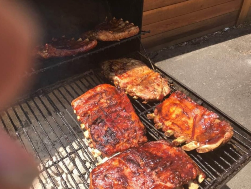 Ribs and sausages are cooking on a grill.