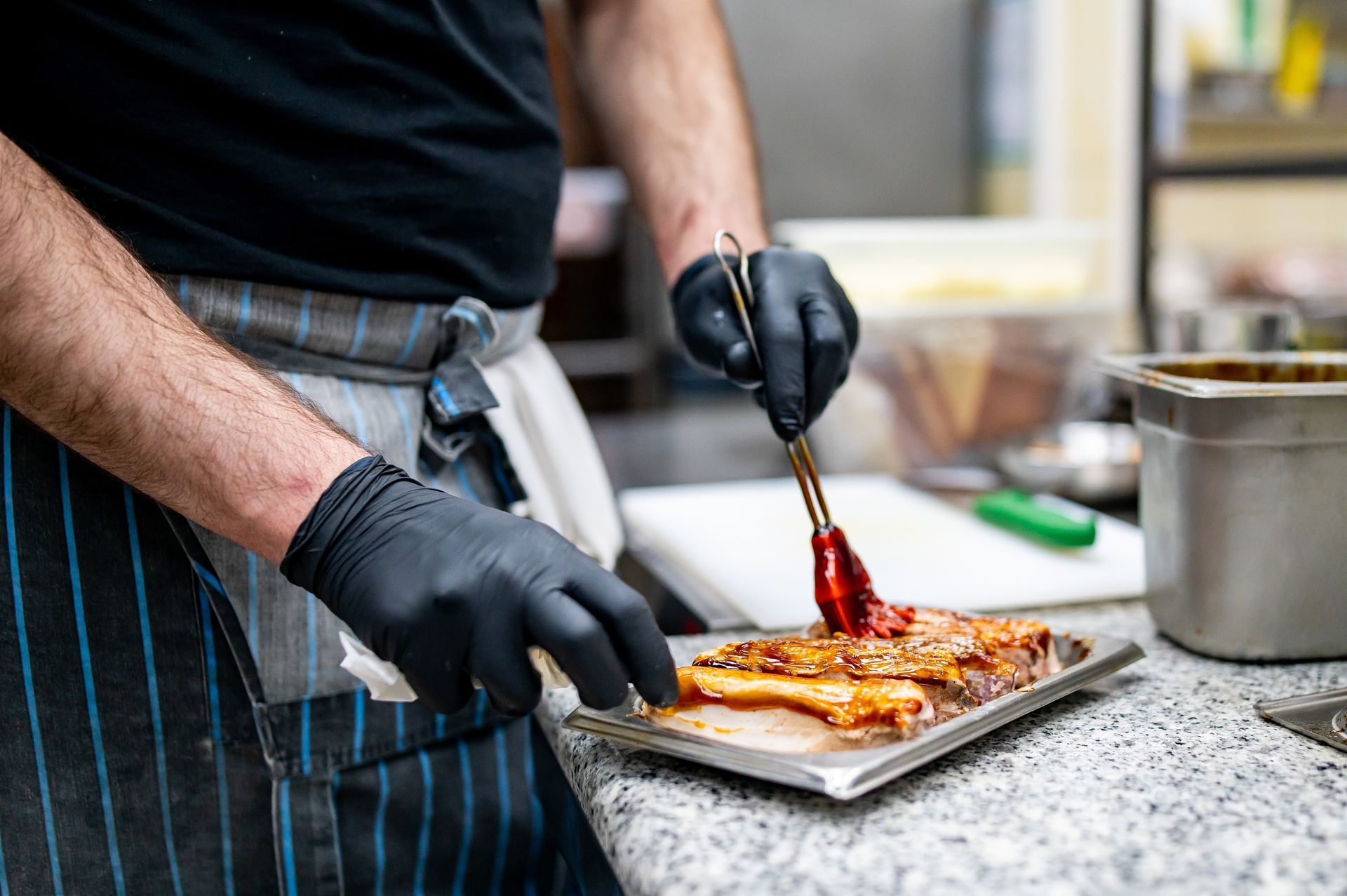 A man wearing black gloves is preparing food on a tray.