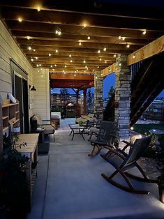 Patio with string lights, seating, stone columns, and view of a yard at dusk.