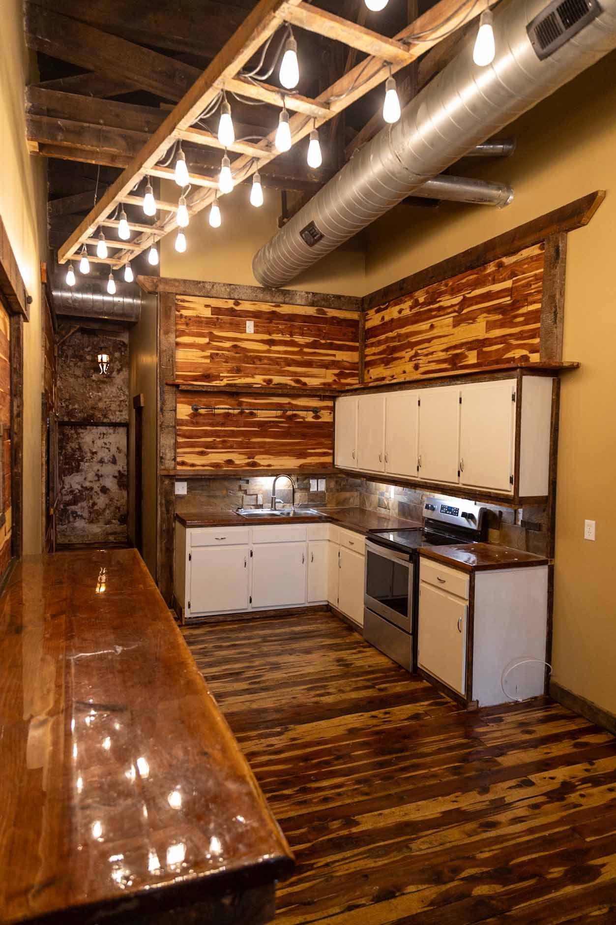 A kitchen with wooden walls , white cabinets , stainless steel appliances and a long wooden table.