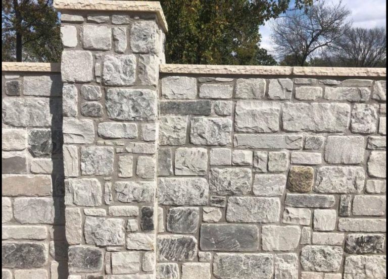 A stone wall with pillars and trees in the background.
