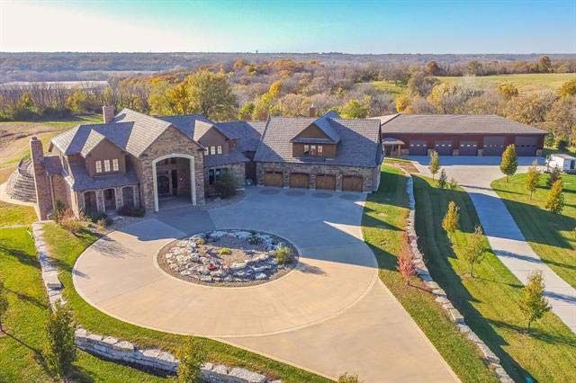 An aerial view of a large house with a large driveway surrounded by grass and trees.