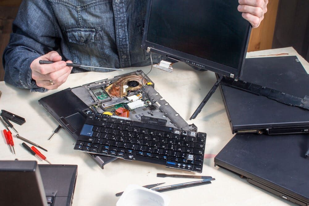a Man is Fixing a Laptop Computer With a Screwdriver — Adaptive PC Solutions in Manoora, QLD