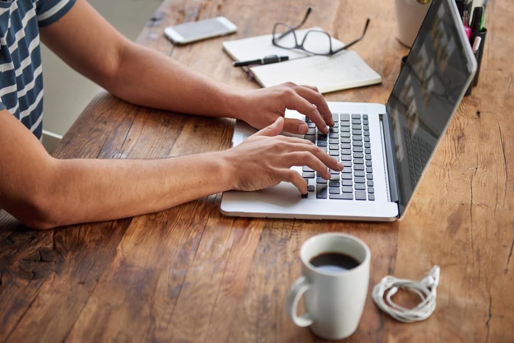 a Person is Typing on a Laptop Computer at a Wooden Desk — Adaptive PC Solutions in Manoora, QLD