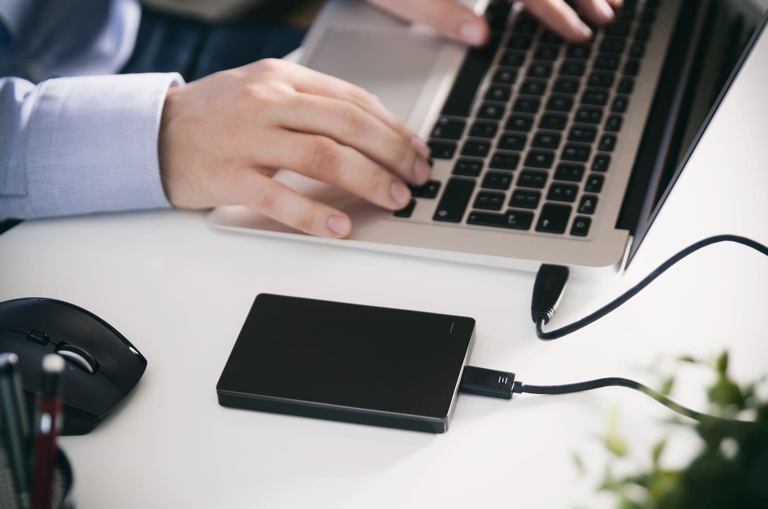 a Man is Typing on a Laptop Next to a Hard Drive — Adaptive PC Solutions In Manoora, QLD
