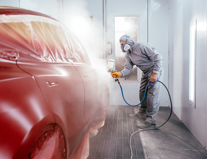 Person in protective suit spray-painting a red car in a paint booth | CARSTAR Oakville West