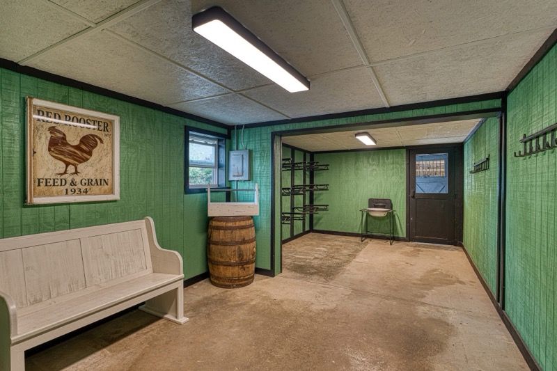 Green-paneled storage room with a bench, a Red Hen sign, a barrel, and shelves.