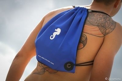 Una donna con un tatuaggio sulla schiena indossa una borsa blu con un cavalluccio marino sopra