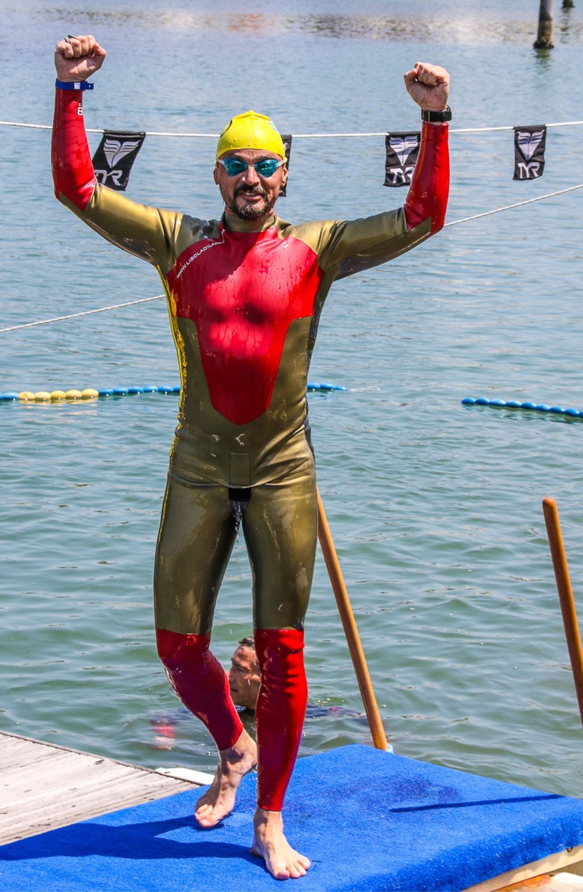 Un uomo con una muta è in piedi su un molo con le braccia alzate.